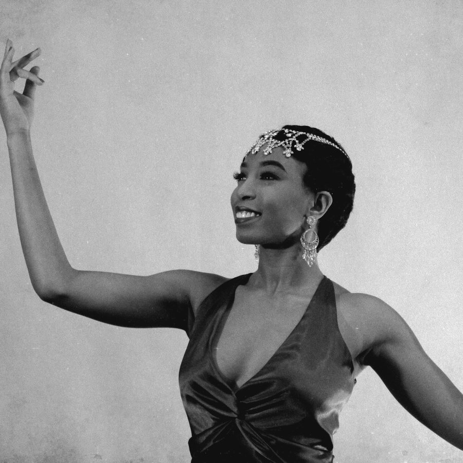 Black and white photo of Aerie mid-dance in a jeweled headpiece, arms raised