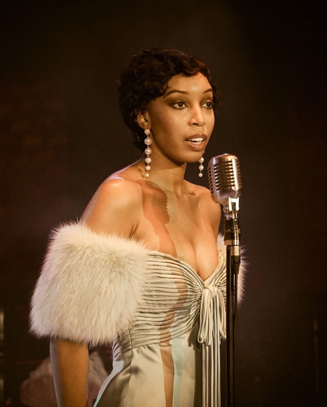 Aerie Williams as Josephine Baker at a vintage microphone, finger waves, pearl earrings and a white fur stole