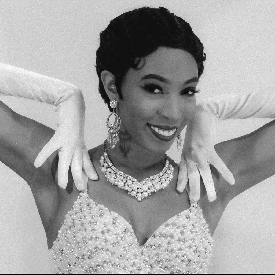 Black and white portrait of Aerie in pearls and long gloves, smiling, hands framing her face